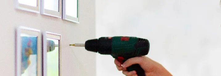 Person bringt mit der Hilfe eines Akkuschraubers Bilder an der Wand an